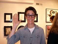 a man wearing glasses is waving in front of some framed pictures