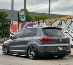 a grey volkswagen suv parked in front of a graffiti covered wall