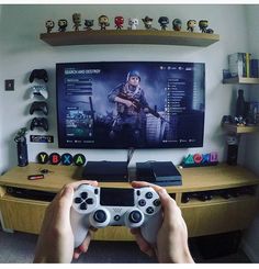 a person holding a video game controller in front of a flat screen tv on top of a wooden entertainment center