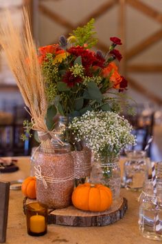 an arrangement of flowers and pumpkins in jars on a table with other items around it