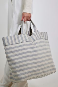 a woman carrying a large gray and white striped tote bag on her left hand