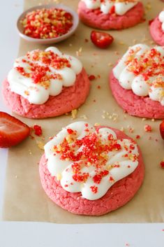 strawberry shortcakes with white frosting and sprinkles on top, next to strawberries