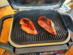 two pieces of meat cooking on top of an electric bbq grill with the lid open