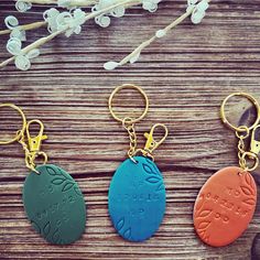 three different colored sand dollar keychains sitting on top of a wooden table