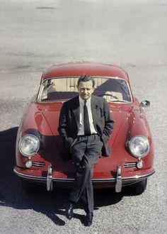 a man in a suit sitting on the hood of a red car