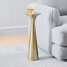 a gold side table with a drink on it in front of a gray couch and white carpet