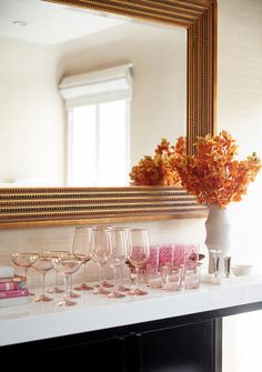 there are many wine glasses on the counter in front of the mirror and vase with flowers