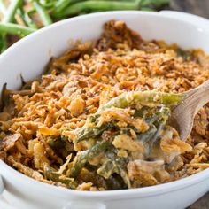 a casserole dish filled with green beans and other vegetables, topped with a wooden spoon