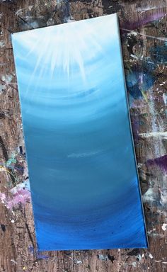 an acrylic painting with blue and white colors on it, sitting on a wooden surface