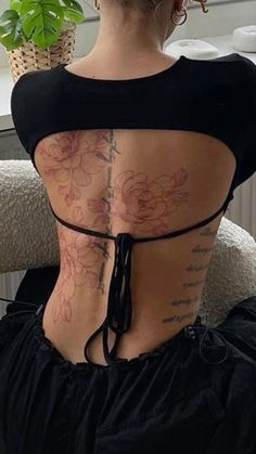 the back of a woman's body with tattoos and flowers on her back, sitting in an office chair