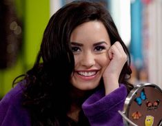 a woman in purple is smiling and holding a hair dryer on her head while sitting down