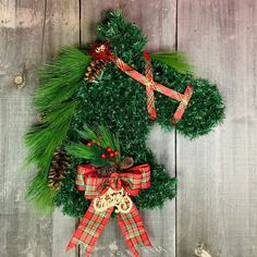 a christmas wreath with pine cones and red ribbon hanging on a wooden wall next to an ornament