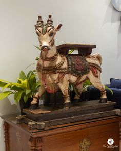 a wooden statue of a goat on top of a table next to a potted plant