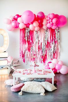 a table topped with lots of pink balloons and tassels next to a mirror