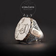 This handcrafted sterling silver men's ring features a unique customizable initials design, perfect for adding a personal touch. The ring is made from high-quality 925 sterling silver and is adorned with intricate engravings. The center showcases a monogram design, as shown with "N J" initials, but can be personalized with any initials, name, or logo of your choice. The sides of the ring are embellished with a bronze door motif and surrounded by blue micro zircon stones, adding a touch of elegan Formal Silver Monogram Rings, Formal Sterling Silver Ring With Initials, Luxury Silver Initial Ring With Polished Finish, Sterling Silver Rings With Initials For Formal Occasions, Silver Monogram Signet Ring, Sterling Silver Rings With Initials For Formal Events, Luxury Silver Initial Ring Hallmarked, Sterling Silver Initials Rings For Formal Occasions, Luxury Silver Hallmarked Initial Ring