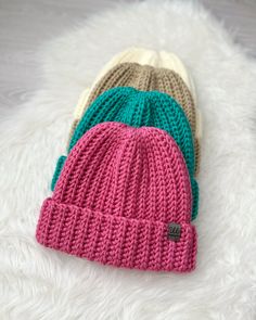 three knitted beanies laying on top of a white furnishing area next to each other