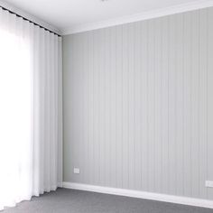 an empty room with white vertical blinds and grey carpeted flooring on the far wall