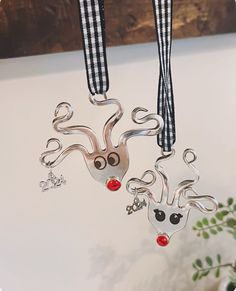 two metal reindeer ornaments hanging from hooks on a white table with black and white gingham checkered ribbon