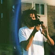 a man with dreadlocks holding a camera in front of his face while standing outside