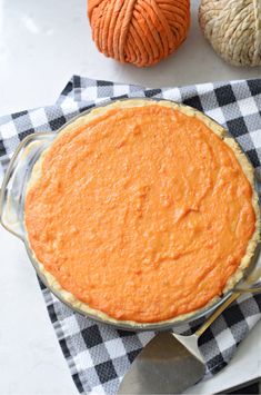 a pie sitting on top of a checkered cloth next to two balls of yarn