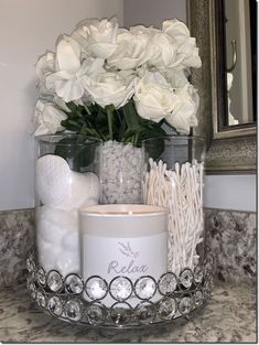 white flowers and candles sit in a glass container on a marble countertop next to a mirror