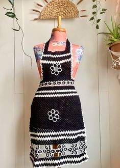 a black and white apron on a mannequin next to a potted plant