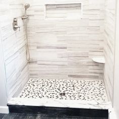 a walk in shower sitting next to a white wall and wooden floored walls with black spots on the floor