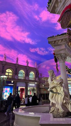 people are standing around in front of a fountain with statues and lights on it at dusk