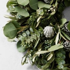 a wreath with pine cones, eucalyptus leaves and other greenery is laid out on a white surface