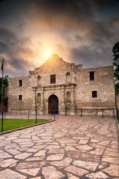 the sun is setting over an old building with stone walkways and cobblestones