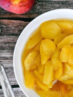 a white bowl filled with sliced fruit on top of a wooden table next to utensils