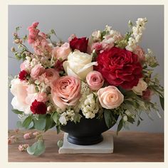 a black vase filled with lots of different colored flowers on top of a wooden table