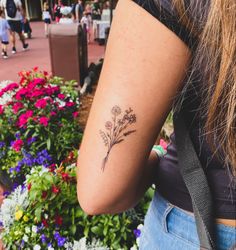 a woman's arm with a flower tattoo on it and flowers in the background