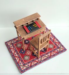 a small wooden desk and chair on top of a rug with a book, pencils, and bookshelf