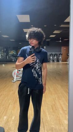 a young man standing on top of a hard wood floor holding a cell phone in his hand