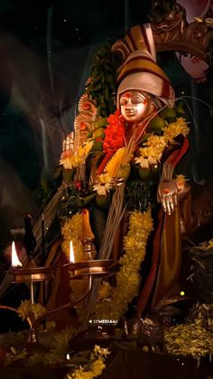 the statue is decorated with flowers and candles in front of a dark background that looks like it has been lit