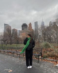 a woman standing in front of a park bench with a green scarf around her neck