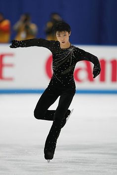 a man skating on an ice rink wearing a black outfit and holding his arms out in the air