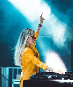 a woman in yellow jacket standing next to a dj's turntable at a concert