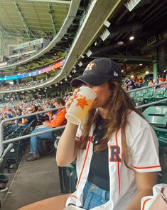 a woman sitting in the stands drinking from a cup