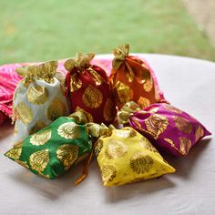 five small pouch bags sitting on top of a white table cloth covered in gold and pink fabric