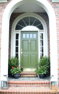 a green front door with potted plants on the steps and an arch above it