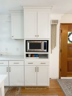 a kitchen with white cupboards and a microwave on top of the cabinet, in front of a door