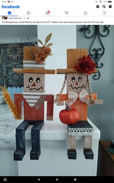 two wooden dolls sitting on top of a white counter next to an apple and pumpkin