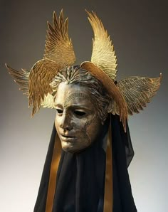 a mask with gold wings on it and a black scarf around its neck is shown in front of a gray background