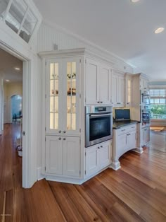 a large kitchen with white cabinets and wood flooring in an open concept home area