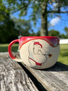 a red and white coffee cup sitting on top of a wooden table next to a tree