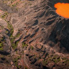 an orange lake surrounded by mountains and grass in the foreground is seen from above