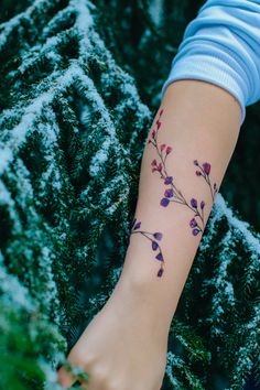 a woman's arm with flowers on it and snow covered trees in the background