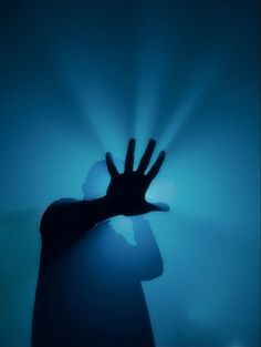 a person holding their hand up in the air with blue light coming from behind them